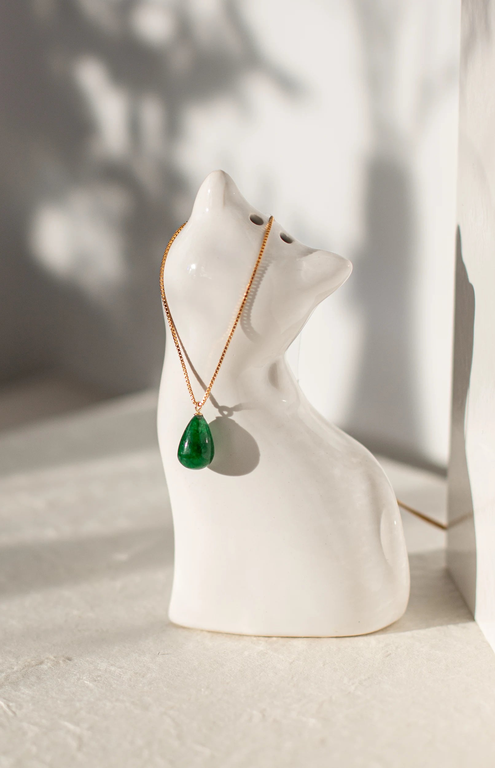 Green teardrop pendant necklace on a white ceramic cat-shaped holder with a blurred background