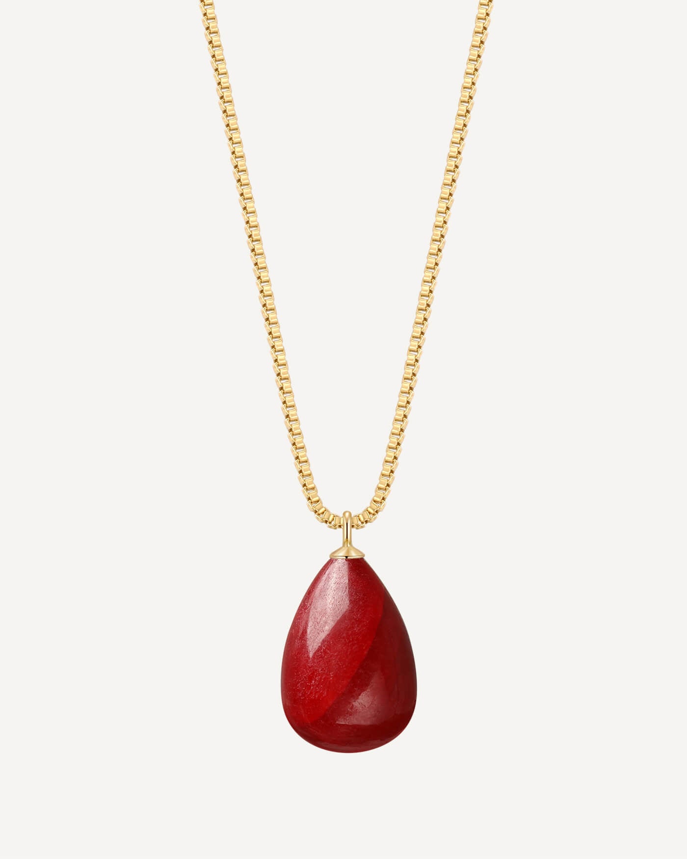 Gold necklace with a red teardrop pendant on a white background
