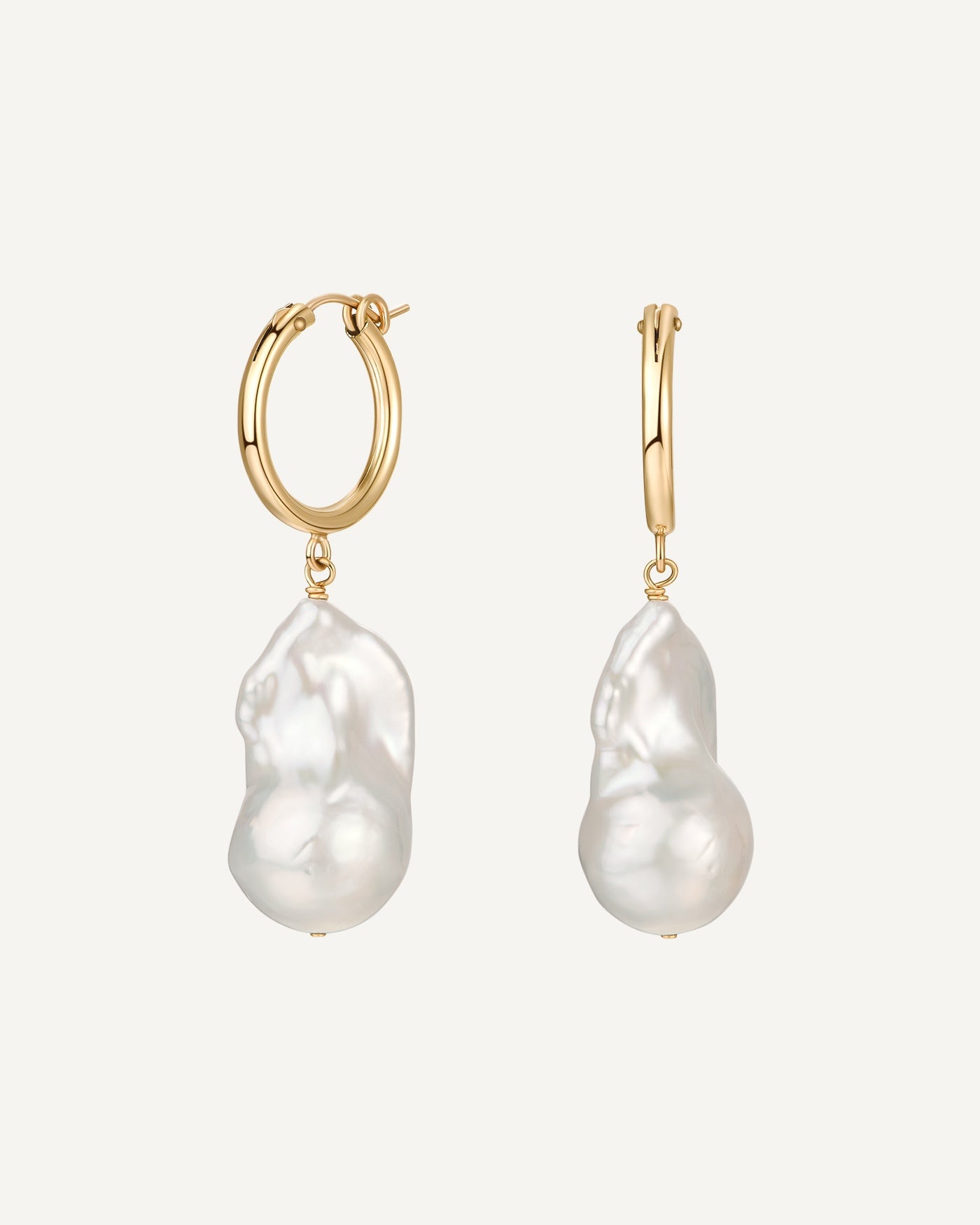 Gold hoop earrings with large white pearls on a light beige background