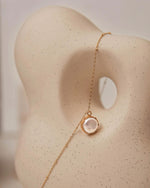 Delicate gold necklace with a rose quartz pendant on a mannequin bust.