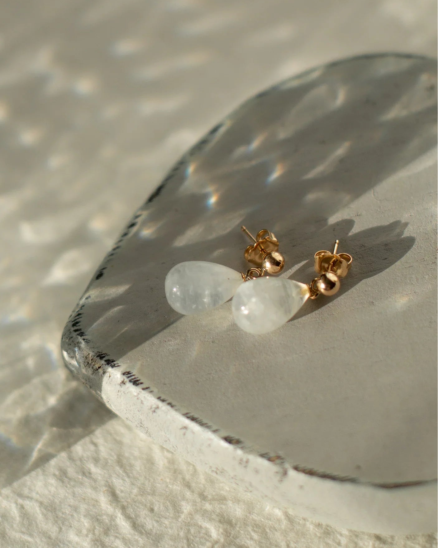 Pair of earrings on a clear stone surface with a neutral background.