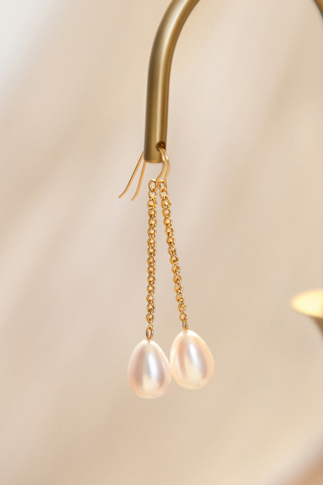 Pearl earrings with gold chains on a light background