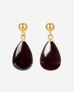 Gold earrings with teardrop-shaped dark red stones on a white background