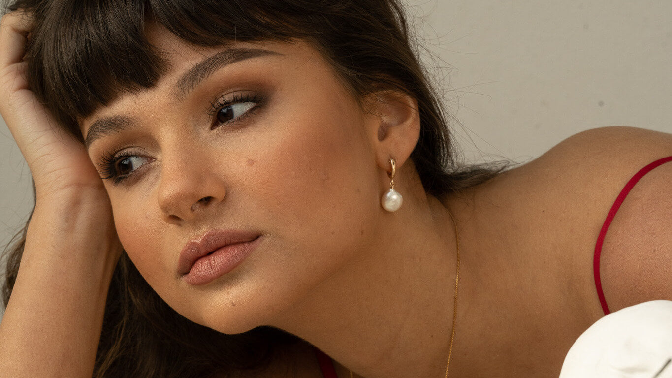 Woman wearing pearl earrings with a neutral background