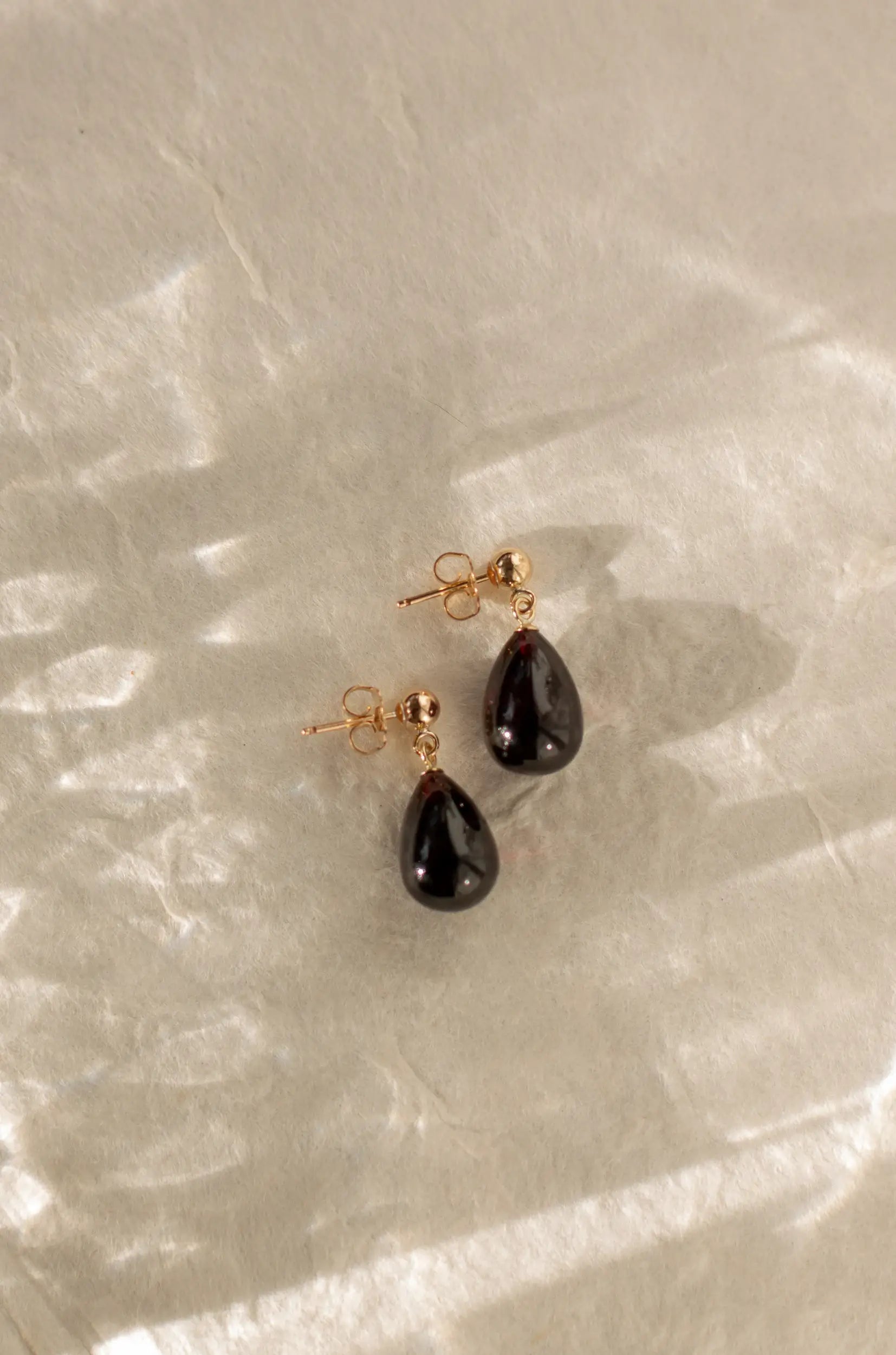Black teardrop earrings with gold hooks on a textured beige surface