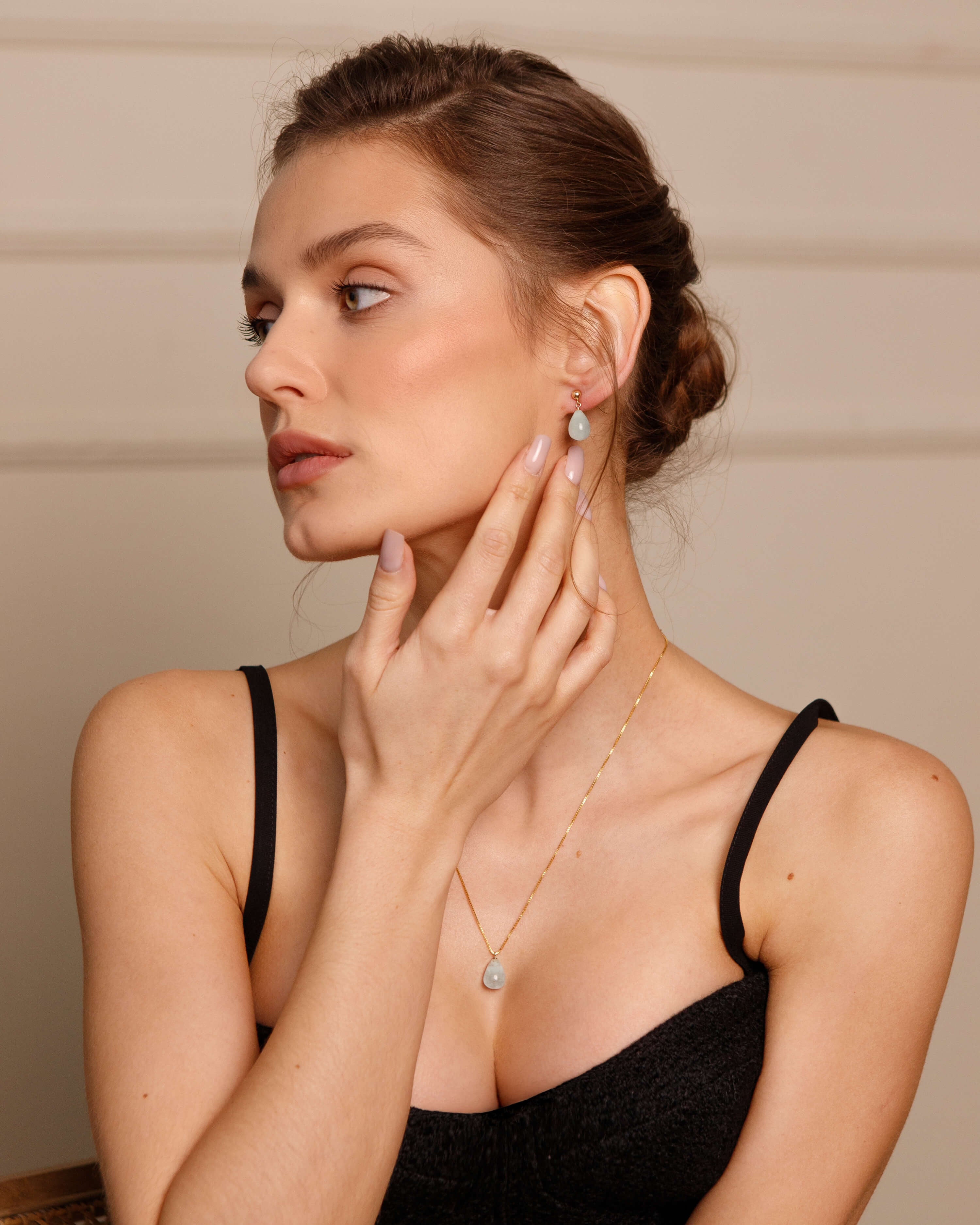 Woman wearing a black top and gold necklace, holding her hand near her face.