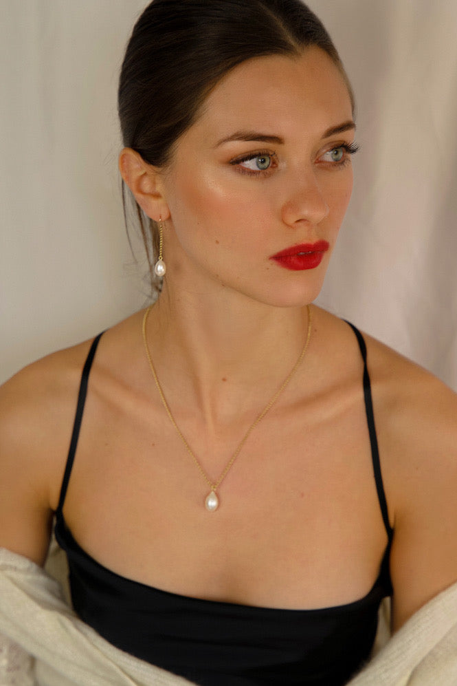Woman wearing a black top with thin straps and a pearl necklace against a neutral background
