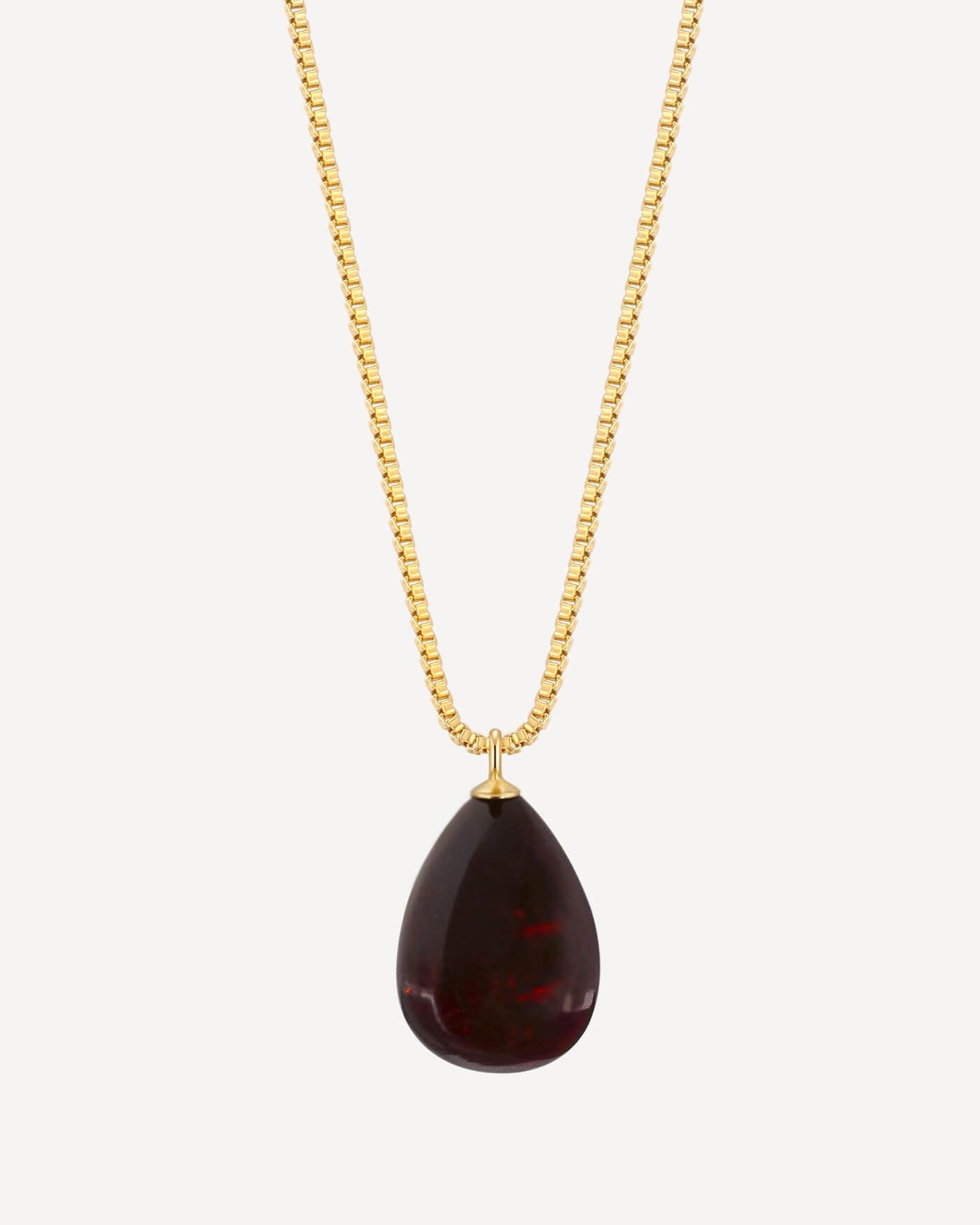 Gold necklace with a teardrop-shaped red pendant on a white background
