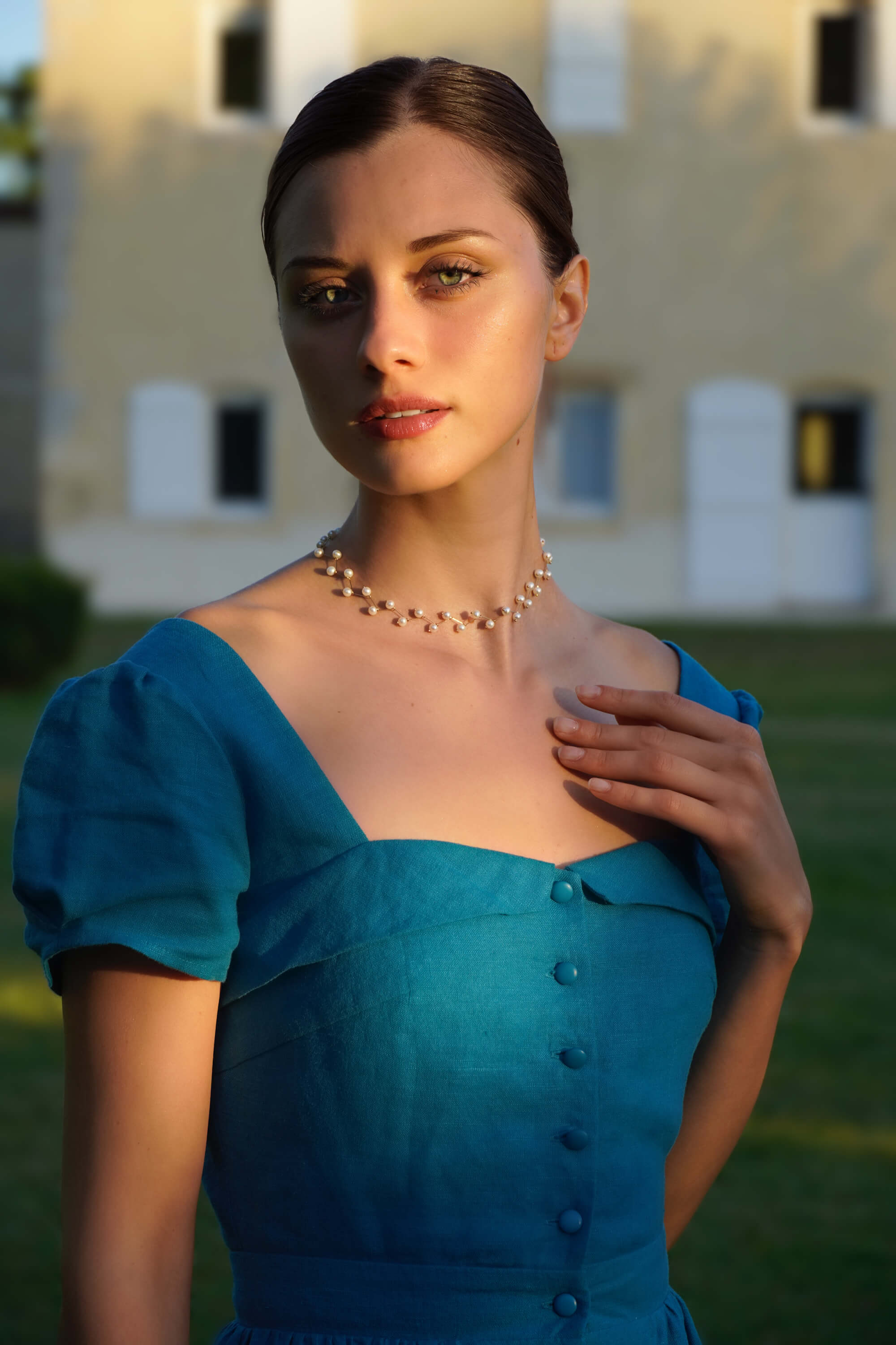 a woman in blue dress is wearing pearl necklace 
