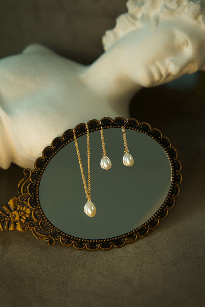 Pearl earrings on a decorative mirror with a marble statue in the background
