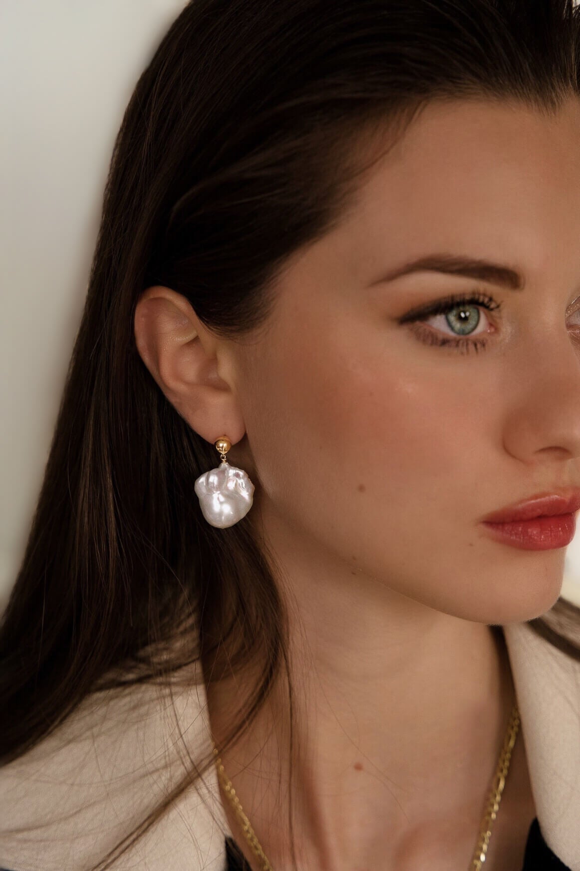 Close-up of a woman wearing pearl earrings with a neutral background