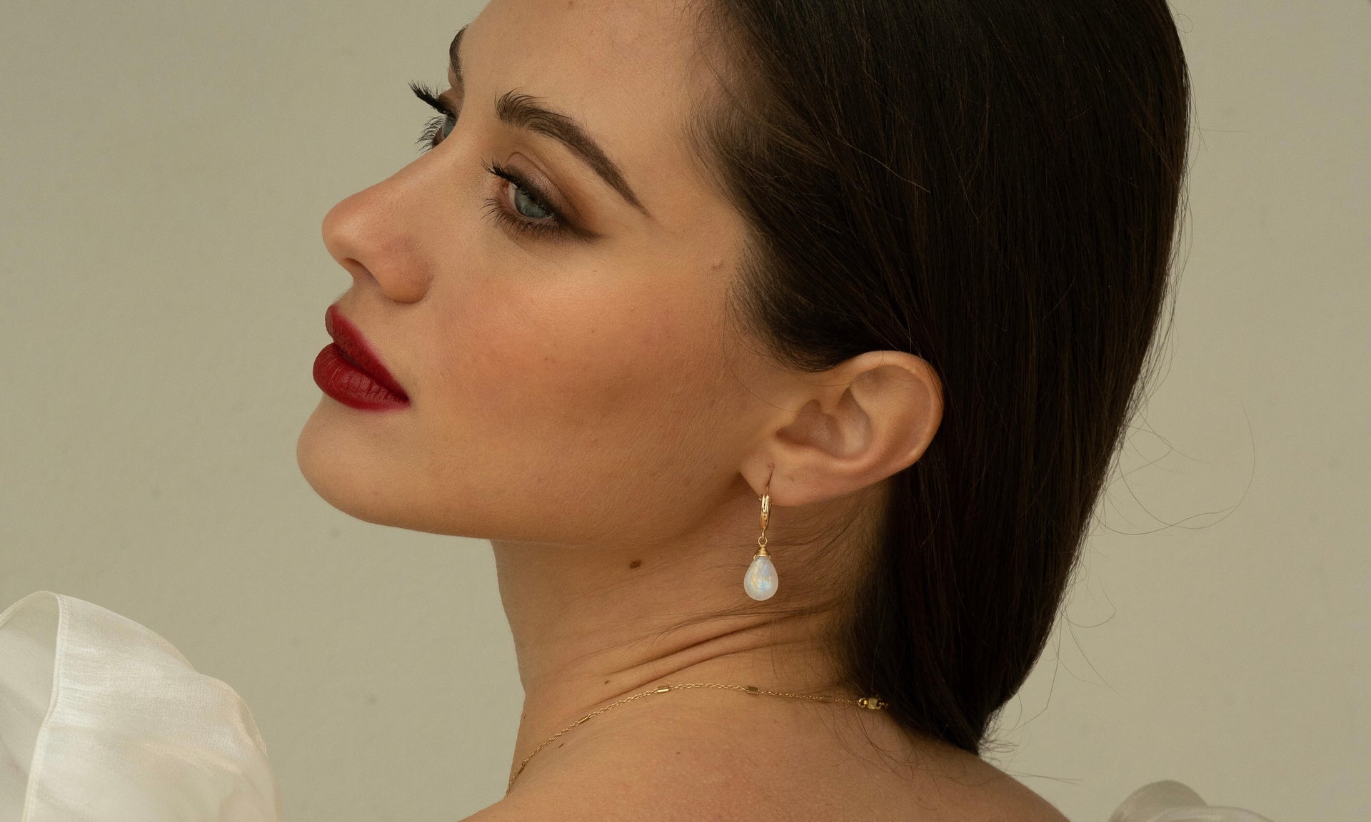 Woman with red lipstick and a white earring against a neutral background