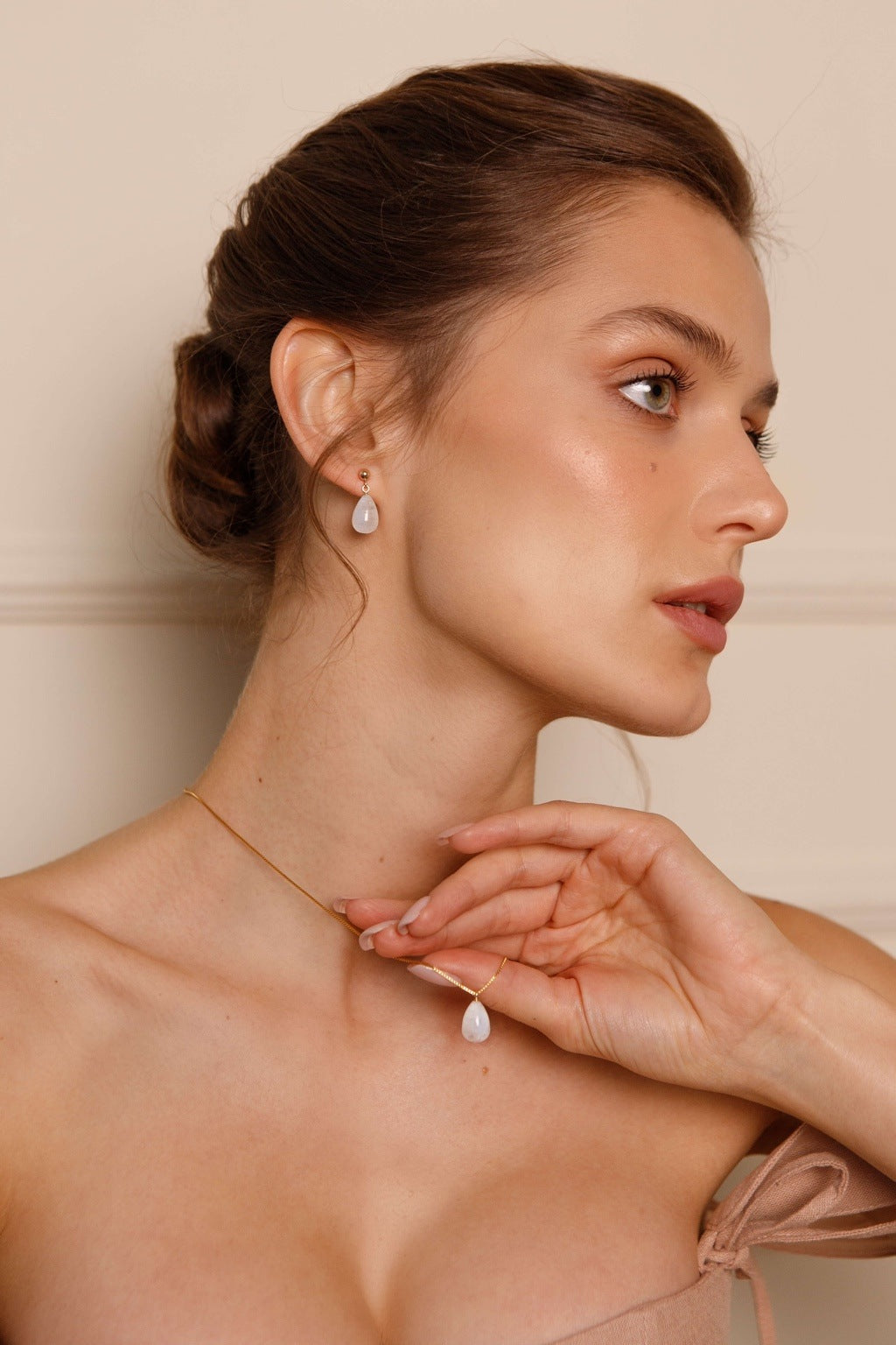 Woman wearing a delicate necklace and earrings against a neutral background