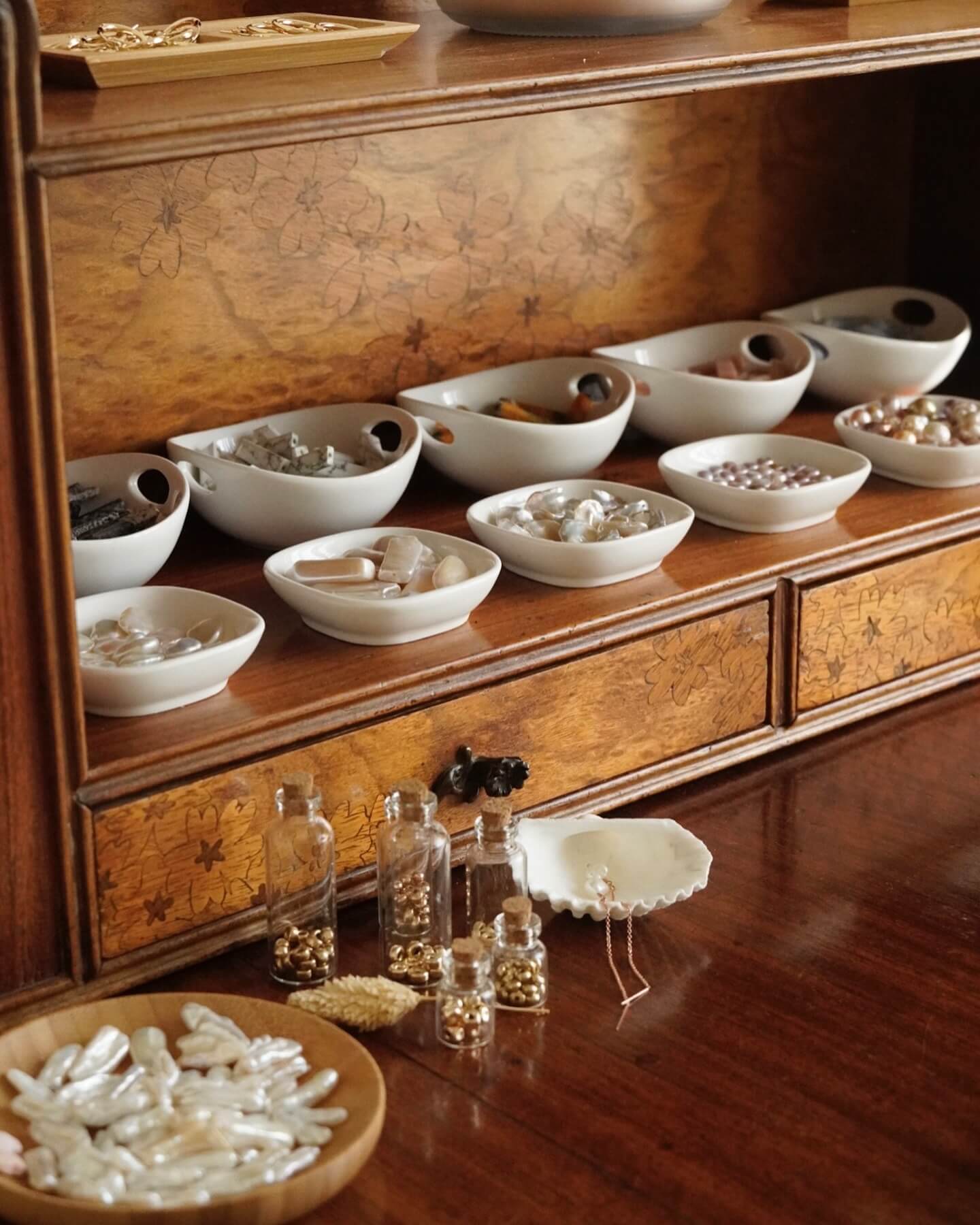 Wooden cabinet with various bowls containing pearls and jewelry on a wooden floor.