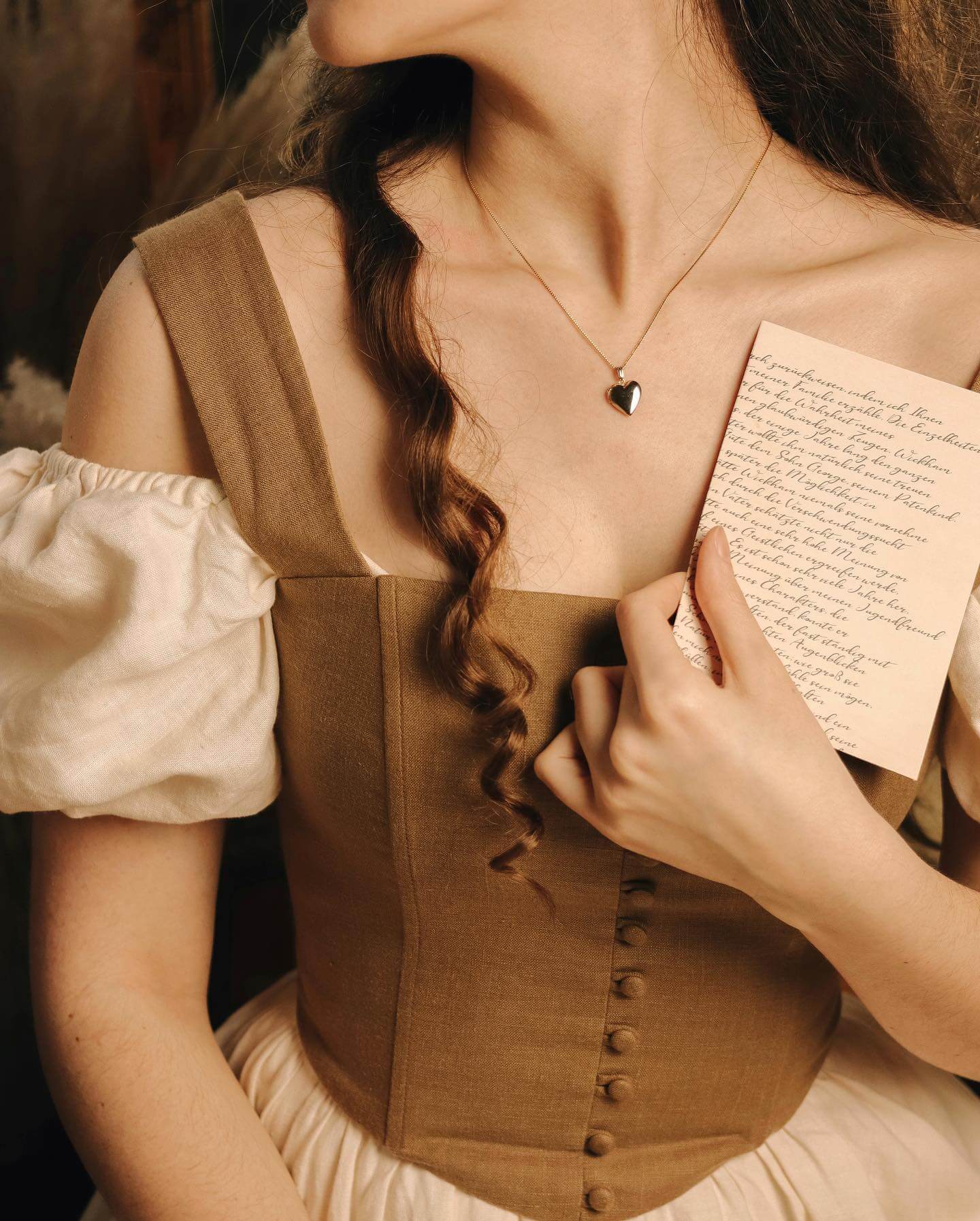 Person wearing a brown corset holding a letter, with a heart-shaped pendant visible.