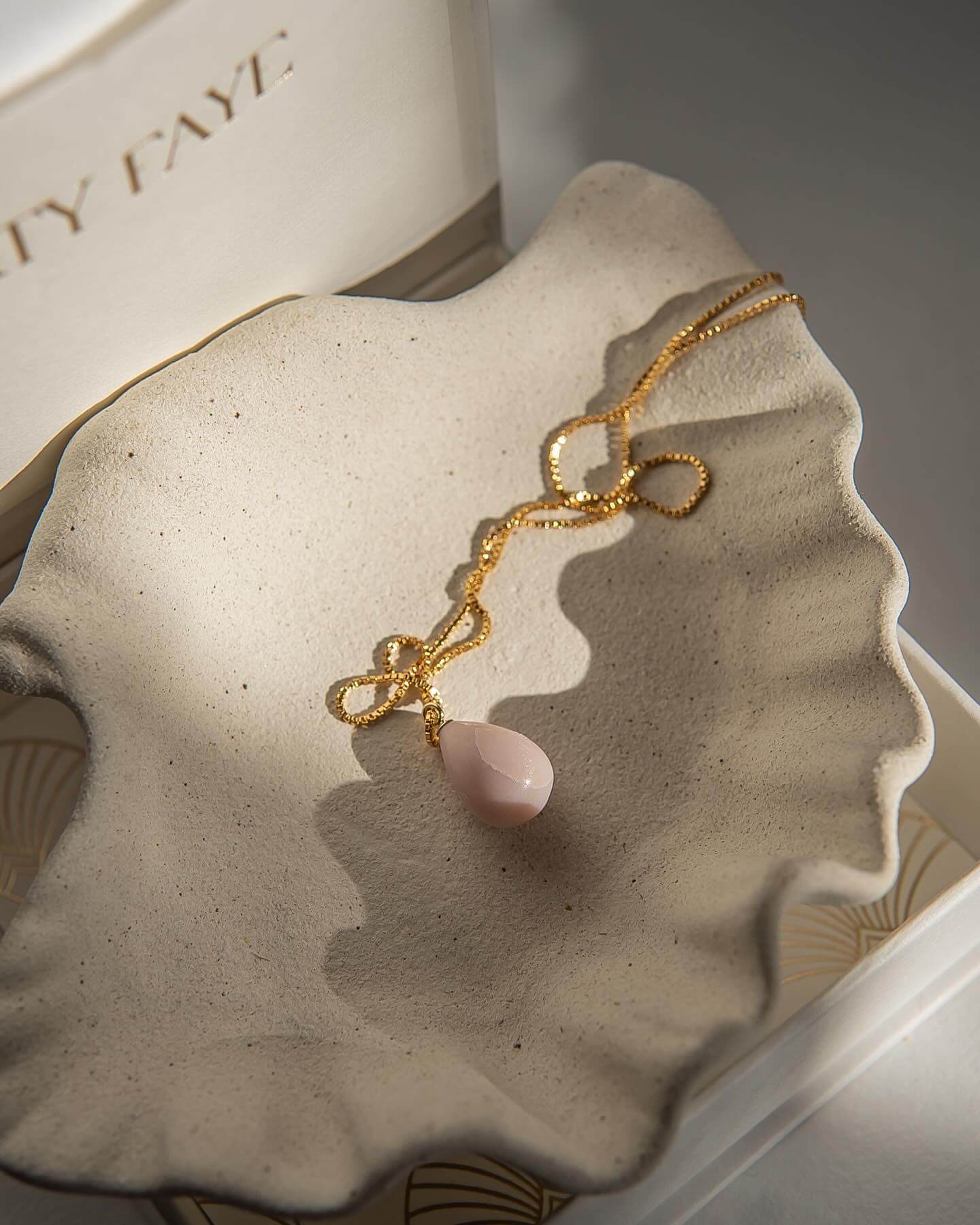 Gold necklace with a pink pendant on a textured surface