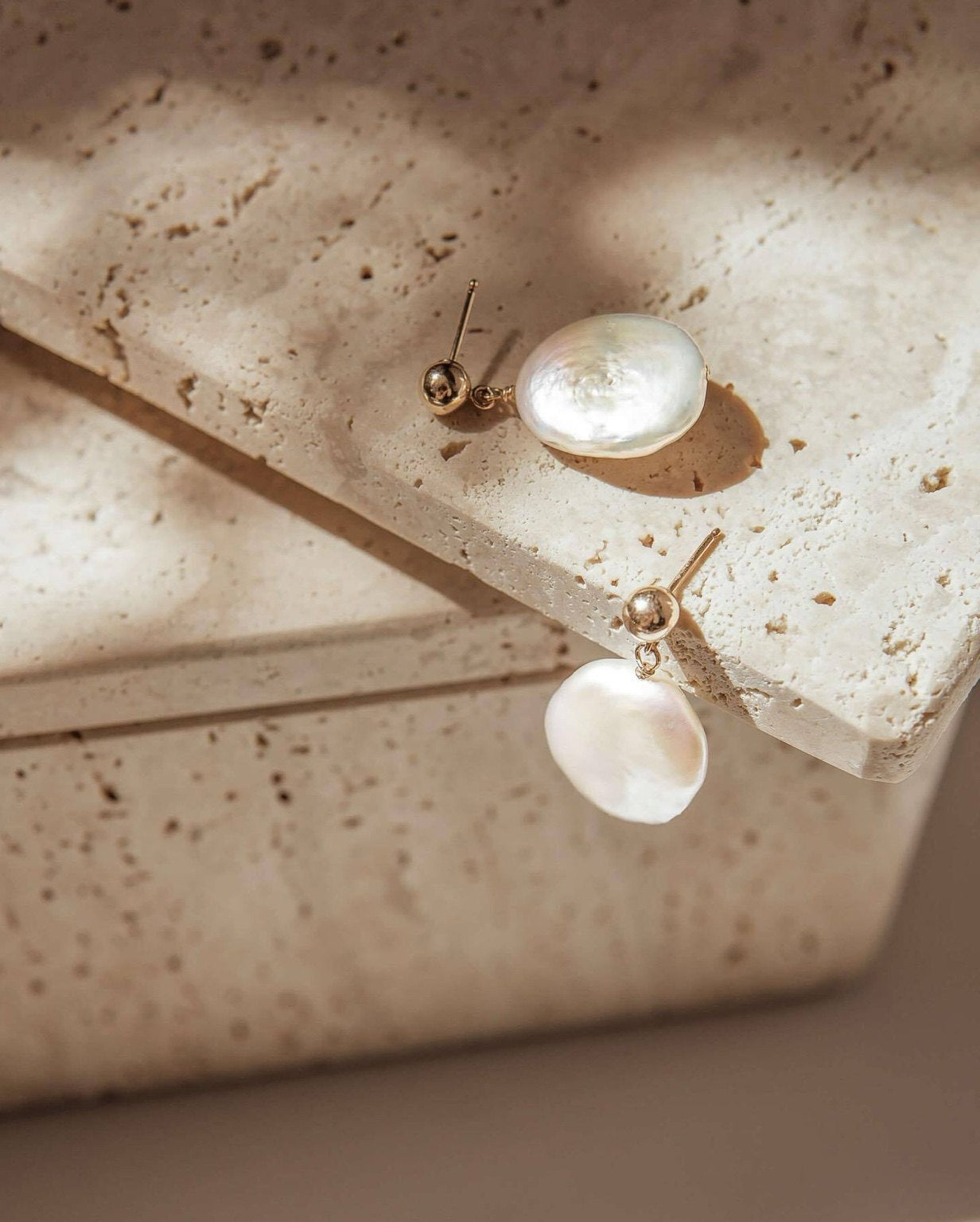 Pearl earrings on a textured beige surface