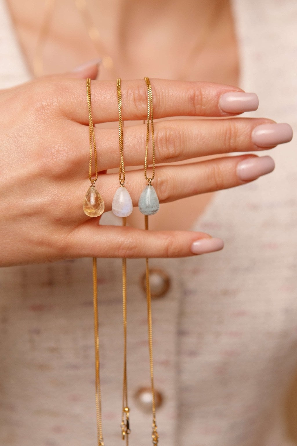 Three gold necklaces with teardrop-shaped pendants on a blurred background