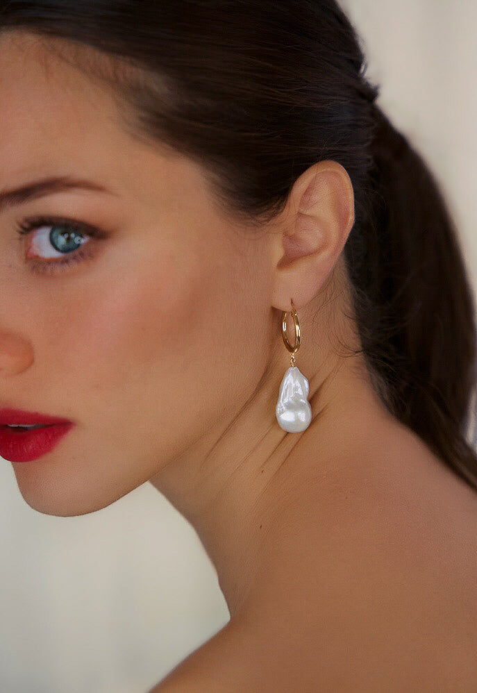 Close-up of a woman wearing a pearl earring with a neutral background